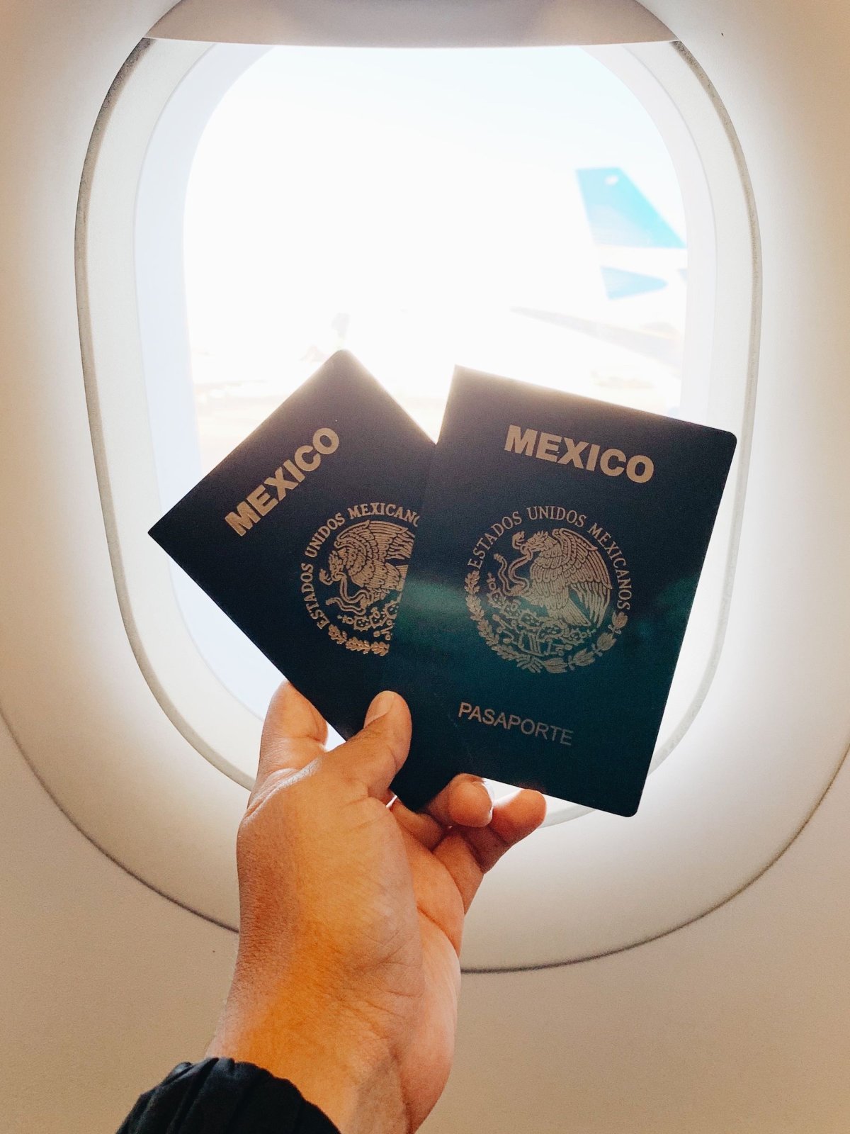 Mão segurando passaportes perto da janela de um avião