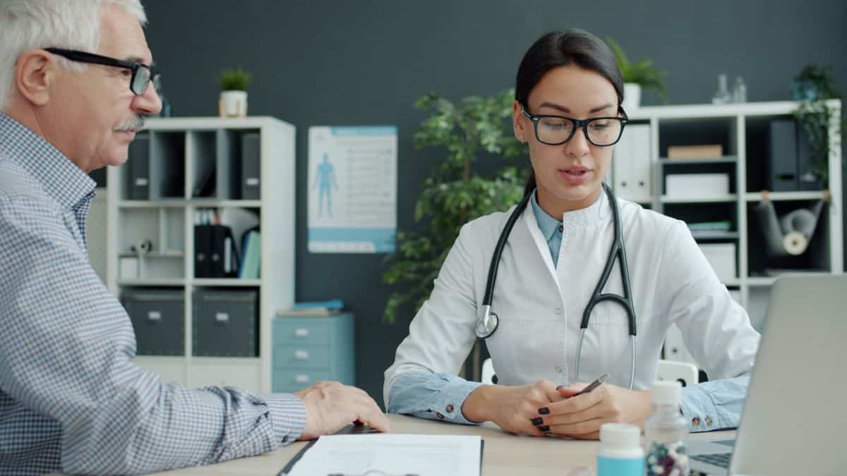 Médico conversando com um paciente idoso em consultório, ilustrando a avaliação da pessoa com deficiência
