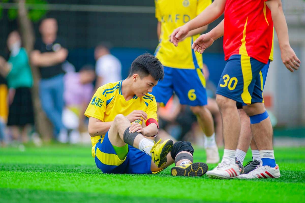 Jogador de futebol sentado no gramado cuidando da perna machucada